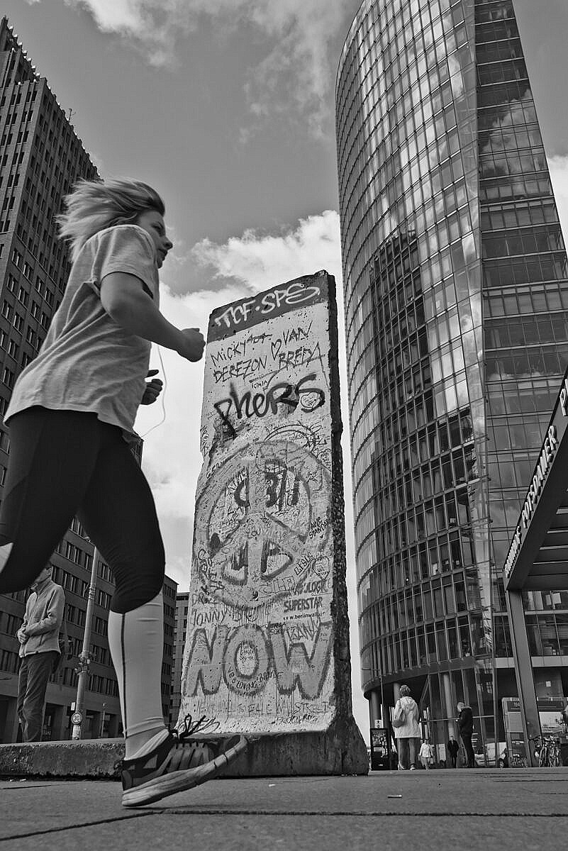 Girl running over the Potzdamer Platz in front of a piece of the Berlin wall