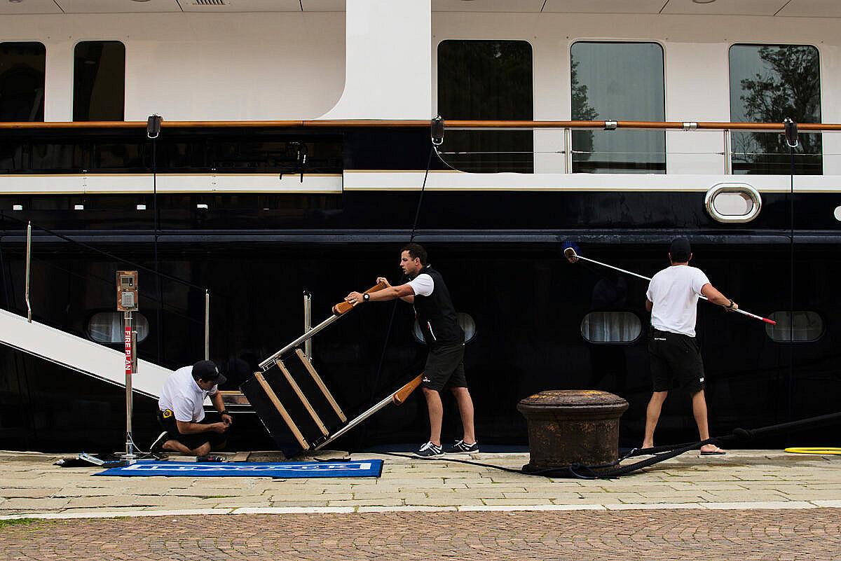 Three sailors occupied with maintenance and cleaning work on a yacht moored in Riva dei 7 martiri in Venice, Italy.