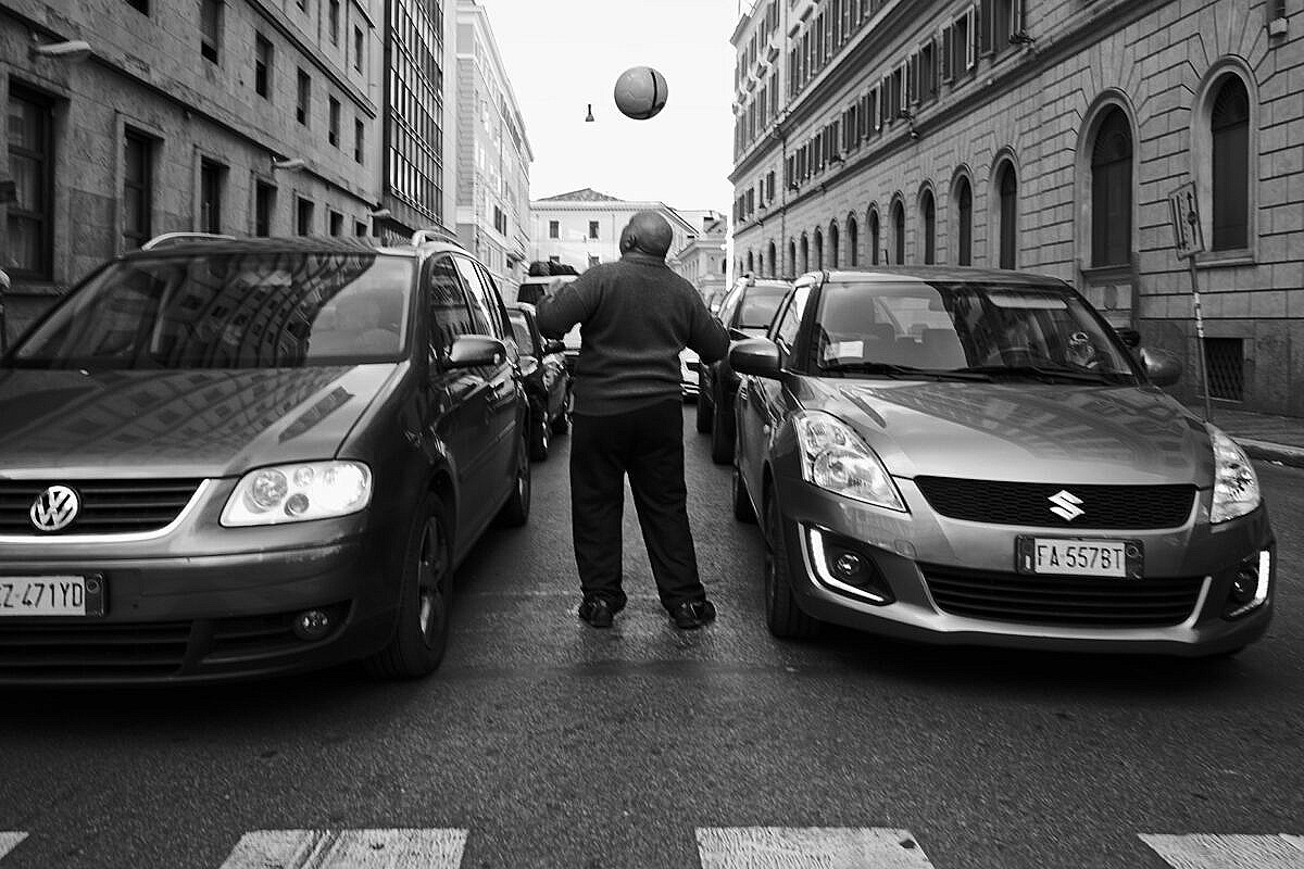 Man playing with a football between waiting cars in Rome.