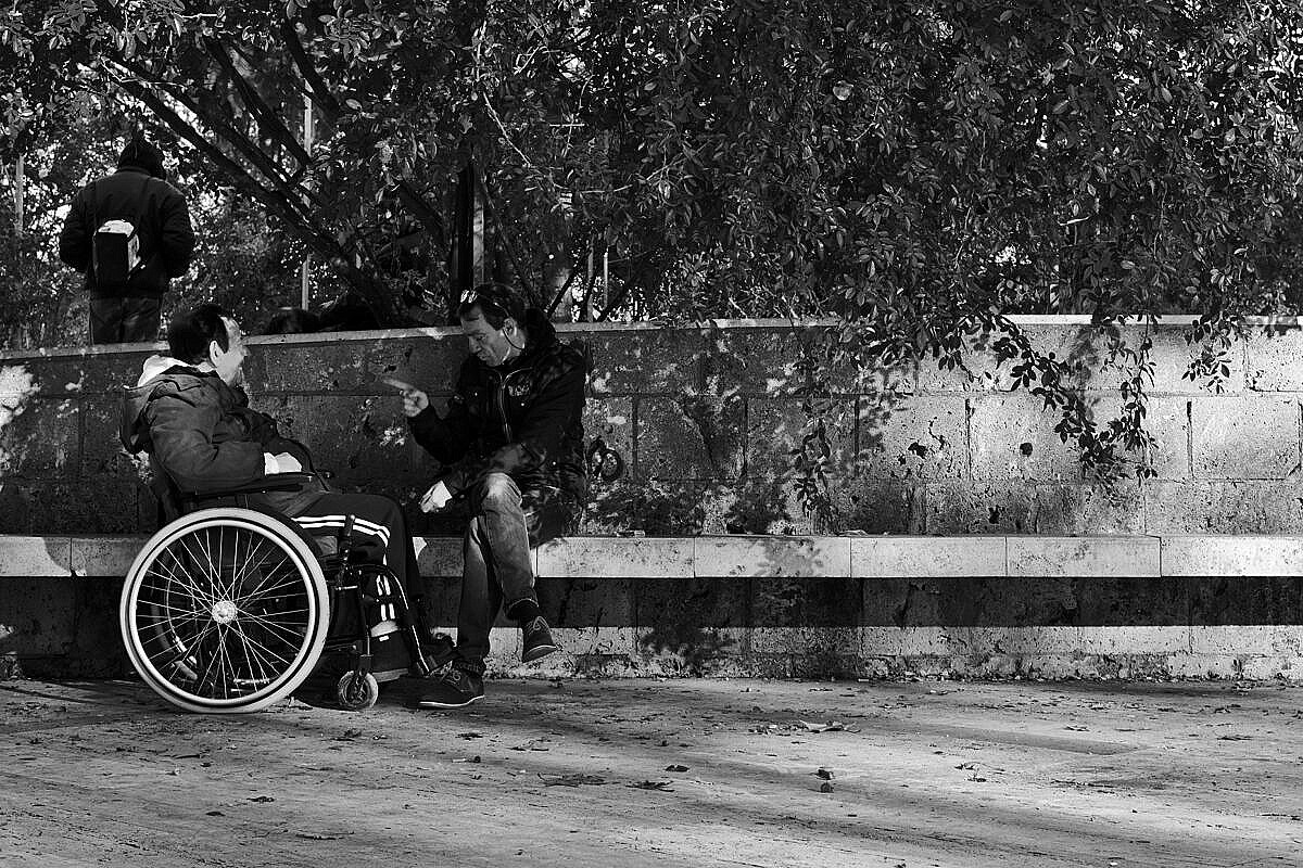 Two people (one in a wheelchair) playing cards and chatting in a park on the Esquiline Hill in Rome