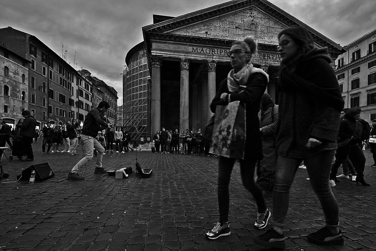 Street musicial playing in front of the Pantheon in Rome with lots of people around.